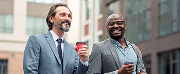 Picture of two businessmans walking outside and holding coffee